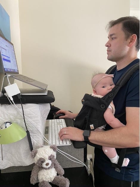 Ryan Brelje at his standing desk with his daughter strapped to his chest