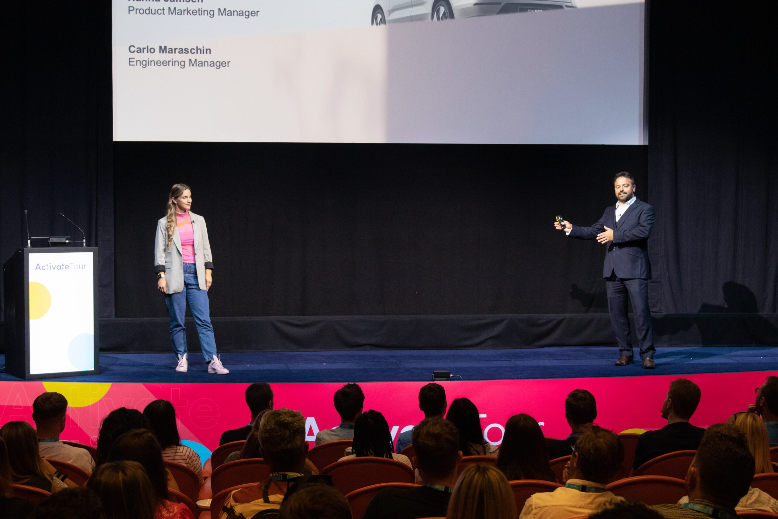 Speakers on a stage, actively presenting to a crowded room.