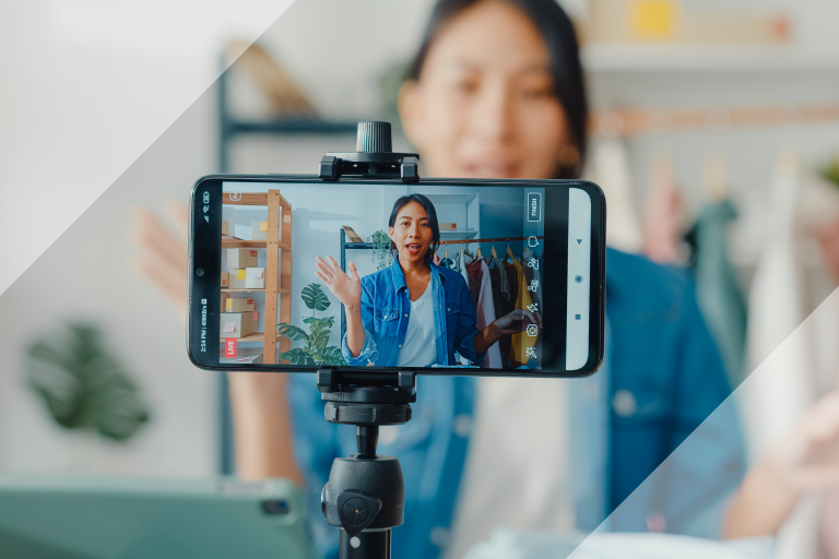 An influencers filming herself. The photo puts the viewer behind the phone, seeing the influencer both on the screen and behind it.