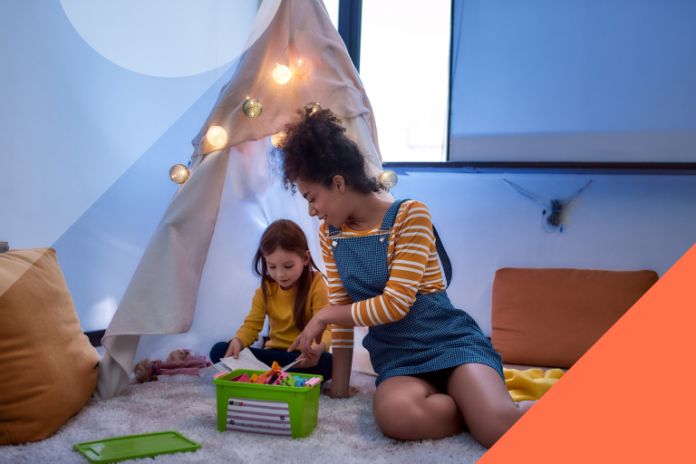 Photo of woman and child sitting on the floor playing with a toy, in front of a play tent